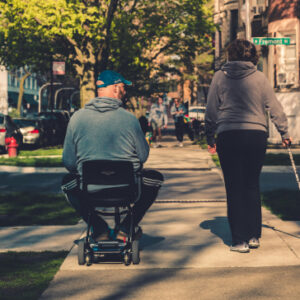 couple,, one walking alongside the other who is using a compact mobility scooterMobility equipment brands UK - couple using compact mobility scooter