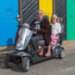 Scooterpac Tandem mobility scooter with elderly couple seated, showing dual seating and front three-quarter view