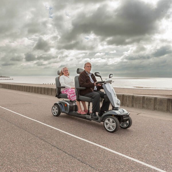Scooterpac Tandem two-person mobility scooter side view with elderly couple riding by seaside