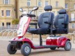 Red Scooterpac Tandem two-person mobility scooter with dual seats, side view on street