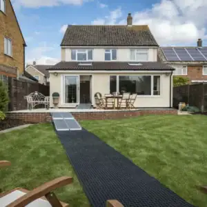 house with a lawned garden and a rolled out track for a mobility scooter to drive over