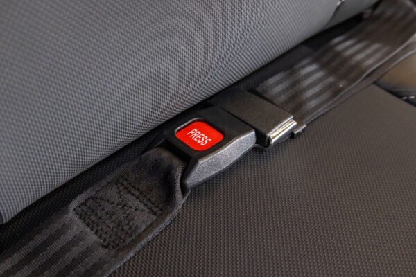 Monarch Super Powerchair seatbelt buckle detail view showing red PRESS release button and black safety strap