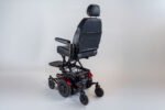 Monarch Super Powerchair in black leather, three-quarter rear view showing elevated seat position and red wheel accents